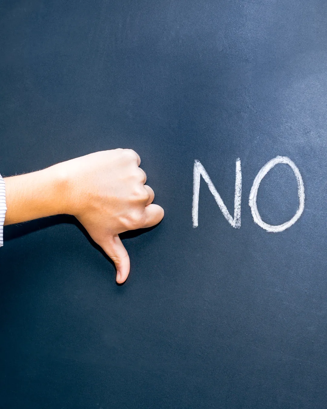 Main au pouce baissé à côté du mot « NO » écrit à la craie sur un tableau