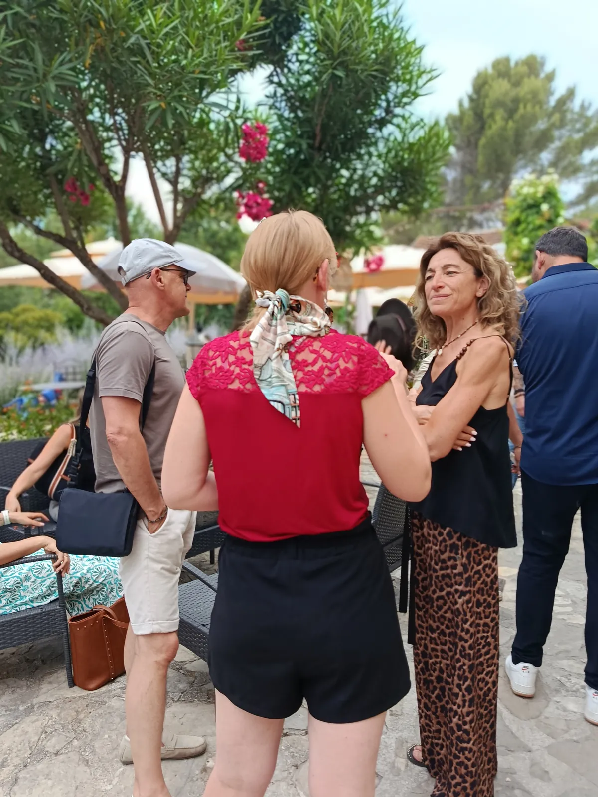 Des participants discutent debout sur une terrasse ombragée, lors d'une rencontre en plein air