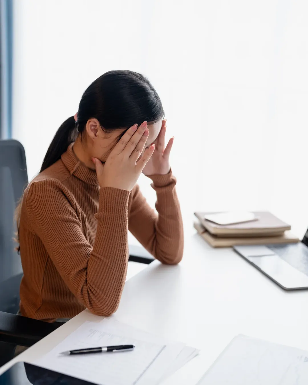 Femme assise à son bureau, le visage dans les mains