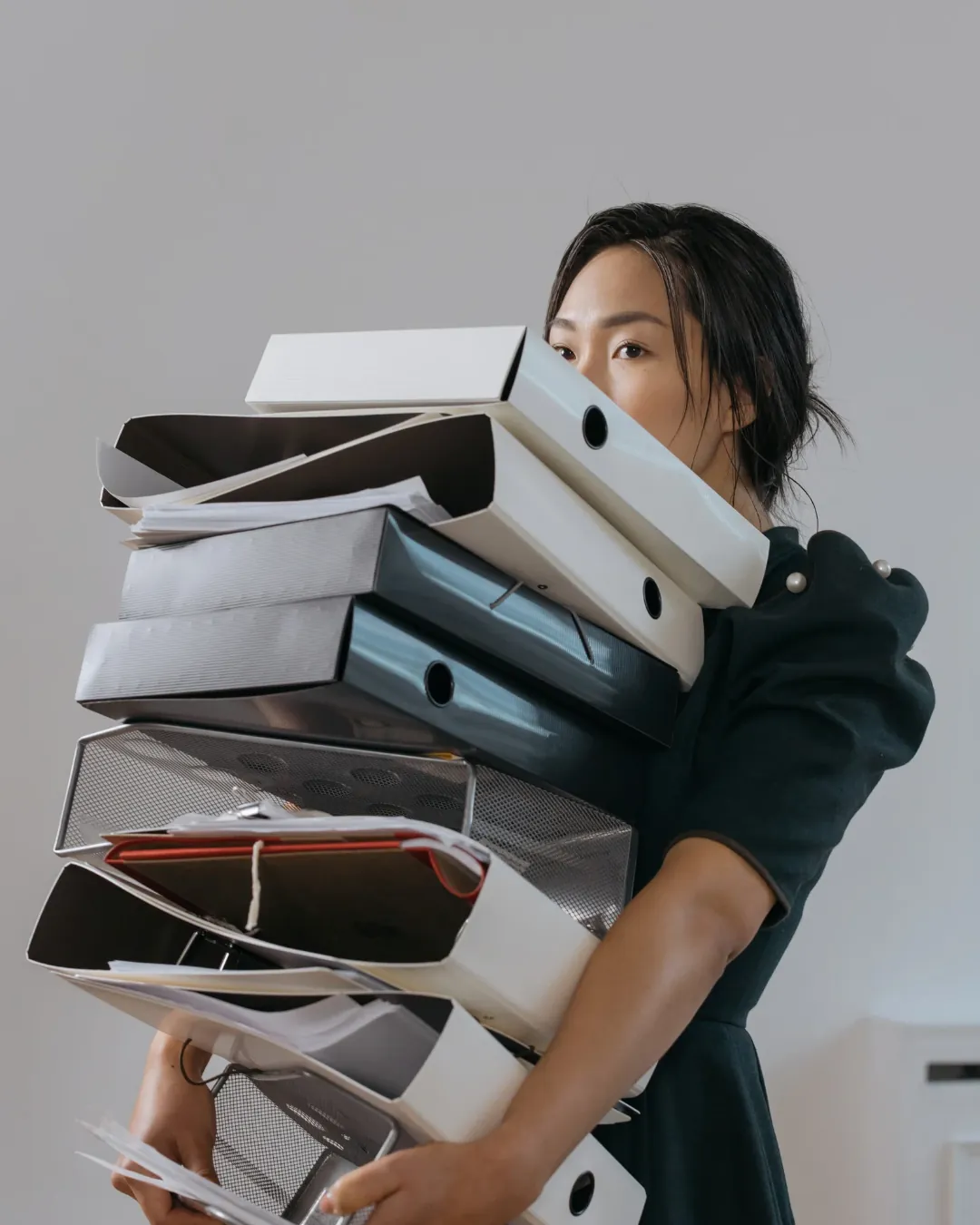 Femme portant une pile de classeurs qui lui cache une partie du visage