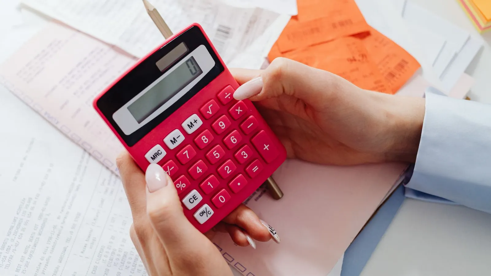 Des mains tiennent une calculatrice rose au-dessus de factures et de tickets.