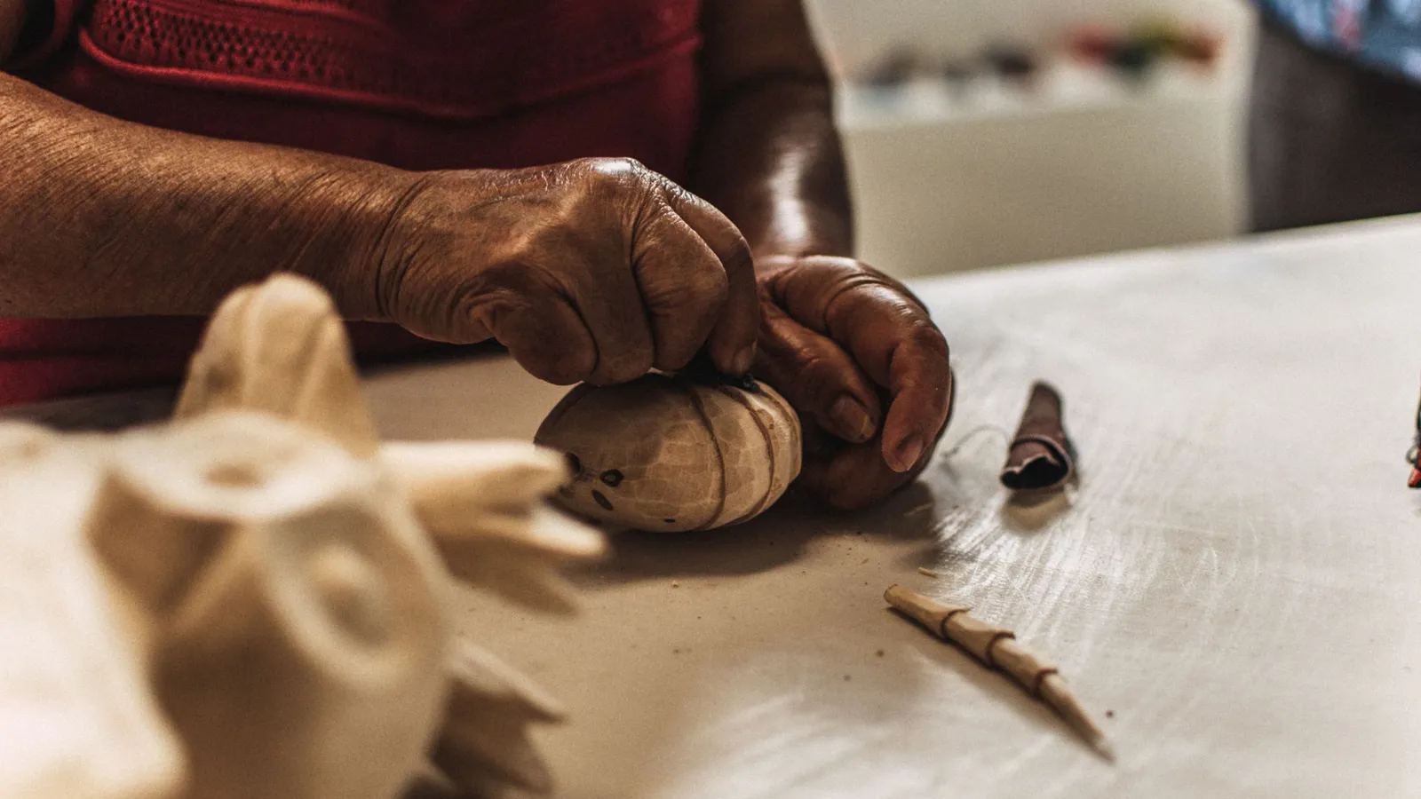 Les mains d'une artisane sculptent une petite pièce de bois sur un établi.