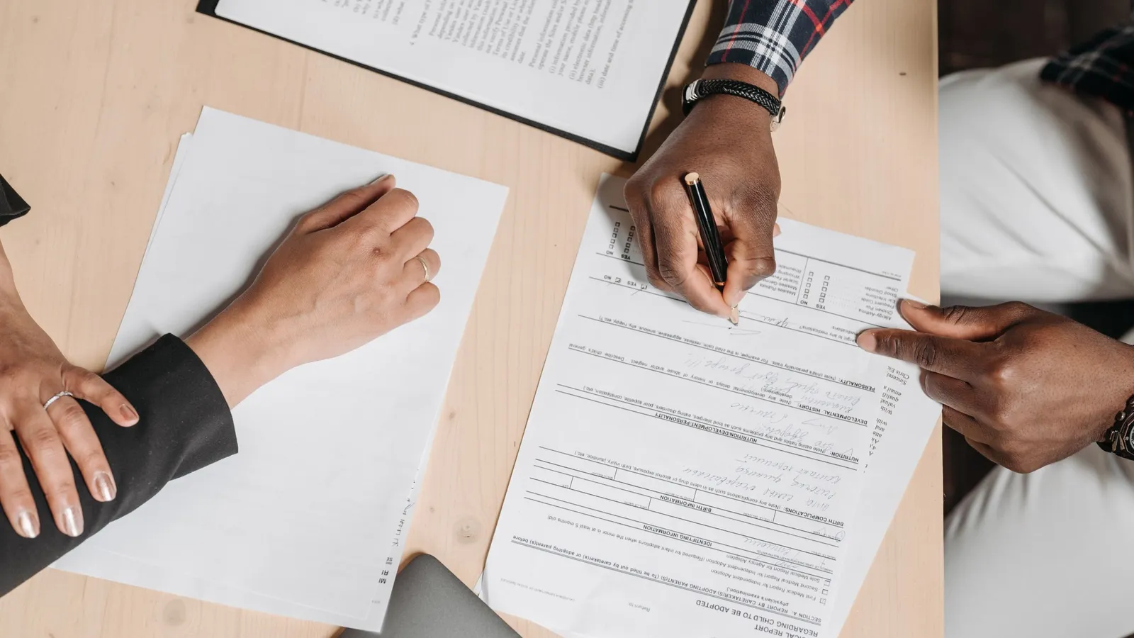 Des mains remplissent des documents posés sur une table claire.