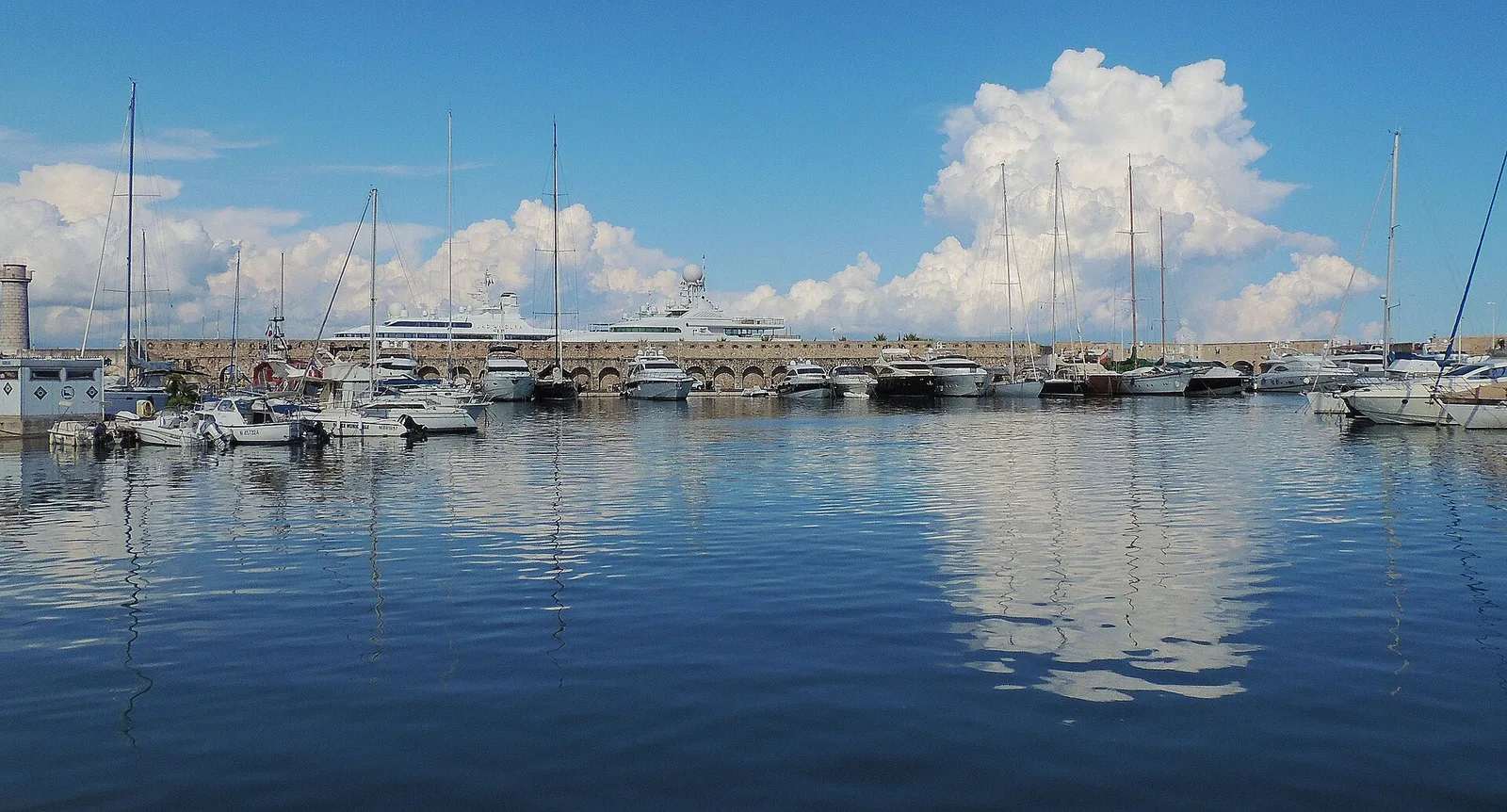 Le port de Saint-Tropez, ses voiliers et ses yachts reflétés dans l'eau calme, le long du môle