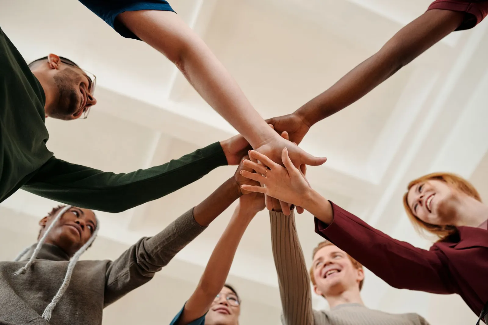 Un groupe diversifié de jeunes adultes formant un cercle uni avec les mains ensemble à l'intérieur.